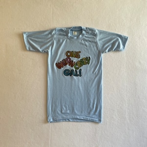 May include: A light blue t-shirt with a rainbow-coloured graphic that says "One Wild N Crazy Gal!"