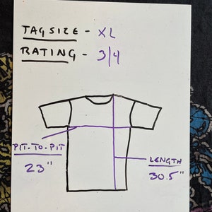 K&ouml;nnte beinhalten: Ein wei&szlig;es T-Shirt mit schwarzem Umriss, das die Ma&szlig;e von Achsel zu Achsel (23 Zoll) und L&auml;nge (30,5 Zoll) zeigt. Die Etikettengr&ouml;&szlig;e ist XL und die Bewertung ist 3/4.