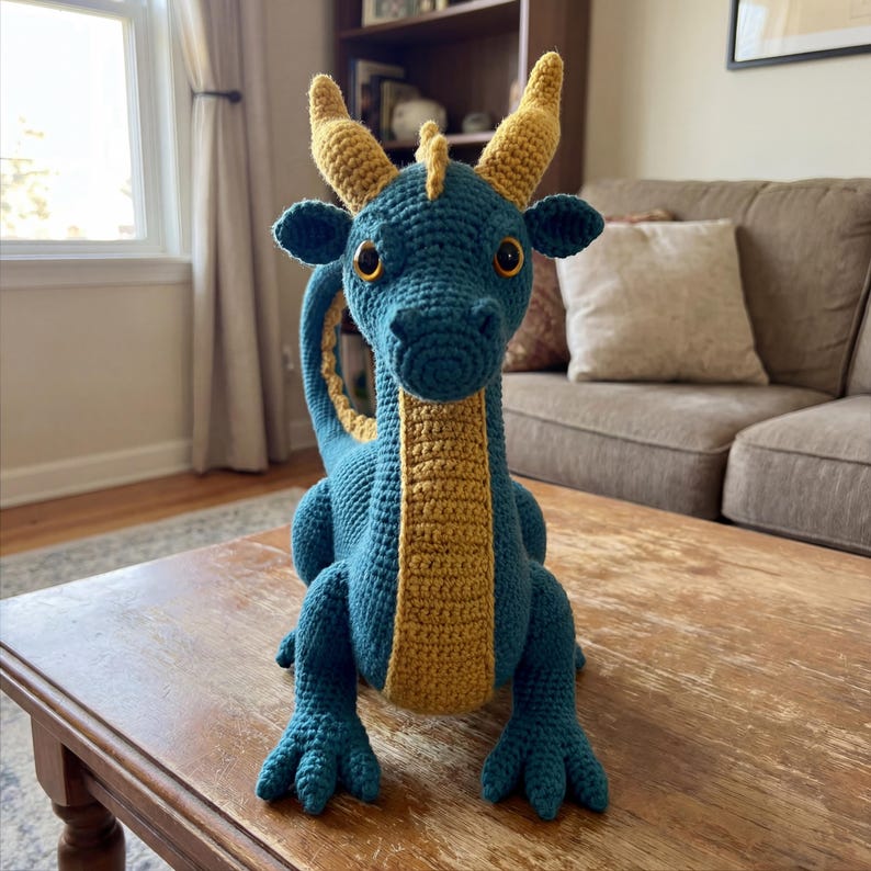 May include: A teal and gold crochet dragon toy with large, round eyes and a long neck. The dragon has yellow horns and a yellow stripe down its chest. The dragon is sitting on a wooden table.