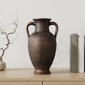 May include: A dark brown, textured amphora-style vase with two curved handles, a flared rim, and a narrow base. The surface features a vertical ribbed pattern with subtle metallic bronze highlights throughout the exterior of the vessel.