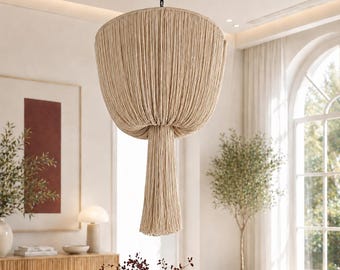 May include: A beige pendant light fixture featuring a wide, bowl-shaped shade constructed from numerous vertical fabric strings. A thick, cylindrical tassel of matching beige strings hangs from the center of the shade, suspended by a black chain.