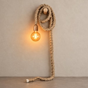 May include: A wall-mounted light fixture featuring a long, thick rope cord coiled around a wooden peg. The rope leads to a metallic socket holding a glowing, round, amber-tinted Edison-style light bulb, with a standard electrical plug at the end.