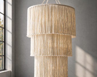 Puede incluir: Un candelabro de tres niveles con un diseño de flecos de color crema. La lámpara cuelga de una cadena en una habitación con una gran ventana arqueada. Los niveles circulares del candelabro disminuyen de tamaño de abajo hacia arriba.