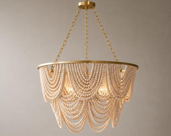 May include: A decorative chandelier with a gold-colored frame and chains. The chandelier features strands of off-white wooden beads cascading in a layered design. The light fixtures are visible within the beaded structure.