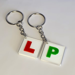 May include: A set of two keychains with a red "L" and a green "P" on white square tags. The keychains are attached to silver key rings.