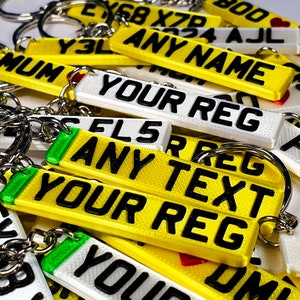 May include: A collection of personalized license plate keychains. The keychains are rectangular, with black text on yellow and white backgrounds. Some keychains read "ANY NAME", "YOUR REG", and "ANY TEXT". Each keychain has a silver keyring.
