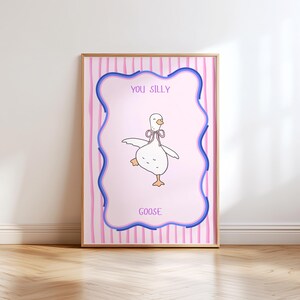 May include: A framed art print featuring a cartoon goose with a pink bow, set against a pink background with blue and pink stripes. The words "YOU SILLY GOOSE" are written on the print.