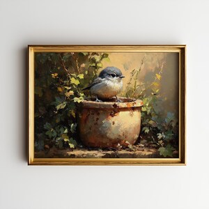 Może przedstawiać: Oprawiony obraz przedstawia małego ptaka siedzącego na zwietrzałej, zardzewiałej doniczce. Ptak ma szare i białe pióra. Obraz ma ciepłą paletę barw z zielonymi liśćmi i złotą ramą.