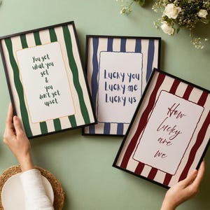 Könnte beinhalten: Drei gerahmte Kunstdrucke mit schwarzen Rändern. Einer hat grün-weiße Streifen mit dem Text "You get what you get & you don't get upset." Ein anderer hat blau-weiße Streifen mit dem Text "Lucky you Lucky me Lucky us." Der dritte hat rot-weiße Streifen mit dem Text "How lucky are we."