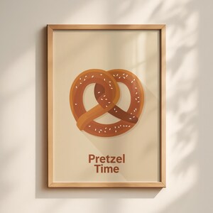 Può includere: Una stampa incorniciata con un'illustrazione di pretzel. Il pretzel è di colore marrone caldo con accenti di sale bianco, su uno sfondo beige. Le parole "Pretzel Time" sono stampate in marrone nella parte inferiore dell'immagine.