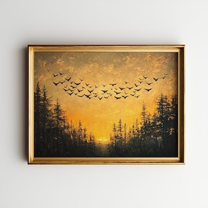 May include: A framed landscape painting depicts a sunset over a forest. Silhouetted trees frame a bright orange and yellow sky, with a flock of black birds in flight. The painting is in a gold-colored frame.