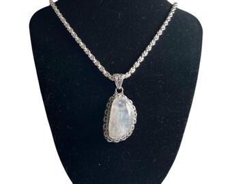 May include: A silver chain necklace with a large, oval-shaped moonstone pendant. The pendant is set in a silver filigree frame.