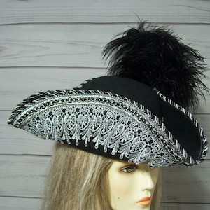 May include: A black felt pirate hat with a silver lace trim and a black feather plume.