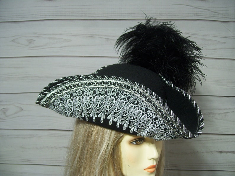 May include: A black felt pirate hat with a silver lace trim and a black feather plume.