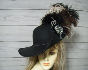 May include: A black felt hat with a wide brim and a feathered plume. The hat is adorned with a black ribbon and a jeweled brooch.