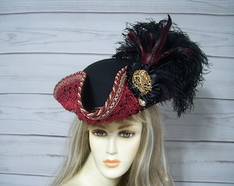 May include: A black felt hat with a red and gold trim, a red feather, and a gold and black jeweled embellishment.