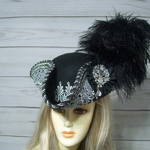 May include: A black felt hat with a silver lace trim and a black feather. The hat has a large, sparkling rhinestone brooch.