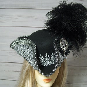 May include: A black felt tricorn hat with a silver lace trim and a black feather plume. The hat has a jeweled embellishment on the side.