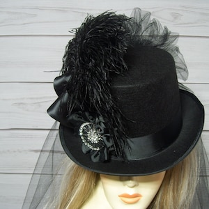 May include: A black top hat with a black feather and a black veil. The hat has a black satin band and a black bow.