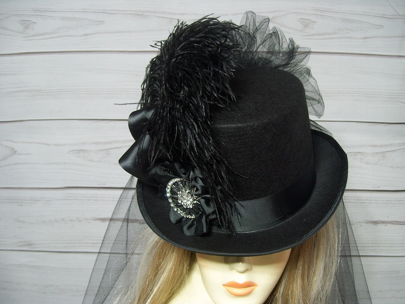 May include: A black top hat with a black feather and a black veil. The hat has a black satin band and a black bow.