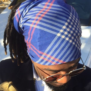 May include: A person wearing a blue and red plaid bandana, sunglasses, a bow tie, and a navy blue jacket. The person is holding a wooden walking stick.
