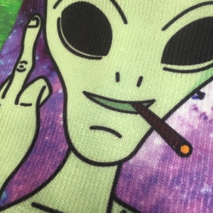 Pair of funky ankle socks printed with a Green Alien smoking a spliff giving the bird on a purple galaxy background.