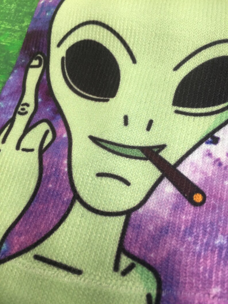 Pair of funky ankle socks printed with a Green Alien smoking a spliff giving the bird on a purple galaxy background.