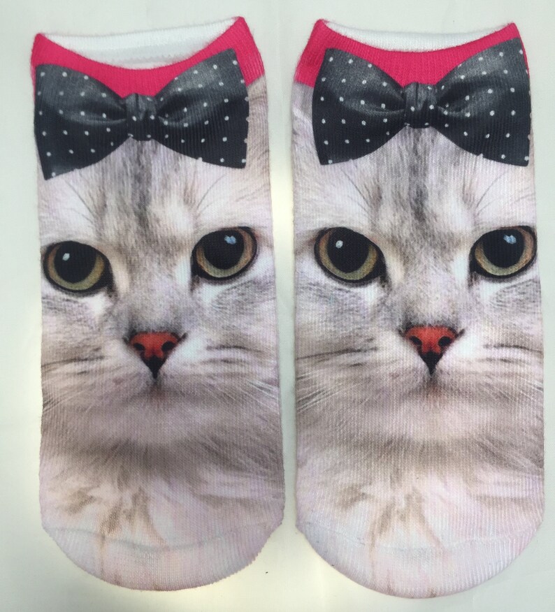 May include: A pair of white ankle socks with a gray cat face and a black bow tie with white polka dots. The bow tie is pink on the top.