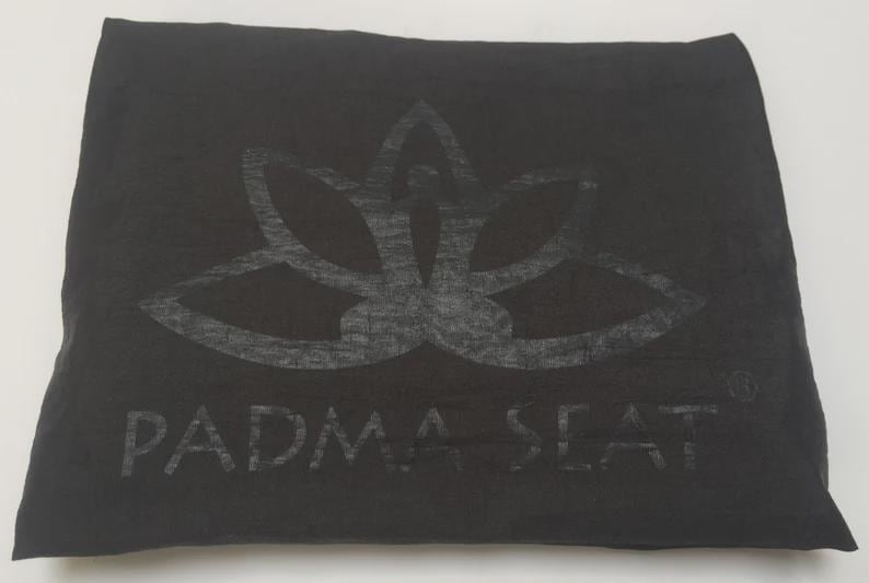 May include: Black meditation cushion with a lotus flower design and the text "PADMA SEAT" printed on the front.