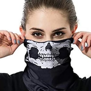May include: Black and white skull face covering. The face covering is made of a soft, stretchy material and features a detailed skull design. The person is holding the face covering up to their face.