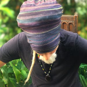 May include: A person wearing a black shirt and pink trousers with a colourful striped hat and a beaded necklace with a large pendant.