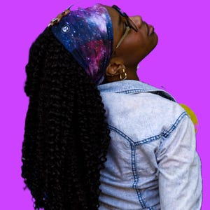 May include: A person with long, curly black hair wearing a galaxy print headband and a light blue denim jacket. The person is looking up and has their head tilted back.