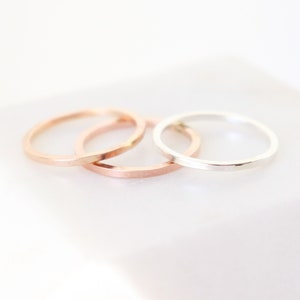May include: Three thin stacking rings, one silver, one rose gold, and one gold.