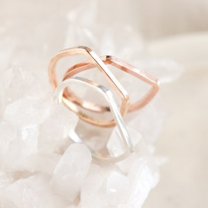 May include: Three geometric rings stacked on top of each other. The top ring is rose gold and the bottom two rings are silver.