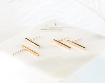 May include: Three pairs of minimalist bar earrings. Two pairs are gold and one pair is silver.