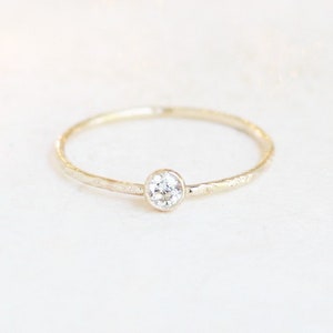 May include: A delicate gold band ring with a single, clear round gemstone set in the center.