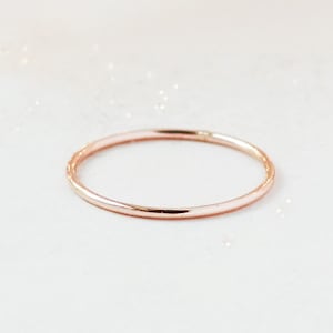 One slim 1 mm rounded finger ring band in 14k rose gold sits on a light off white background.