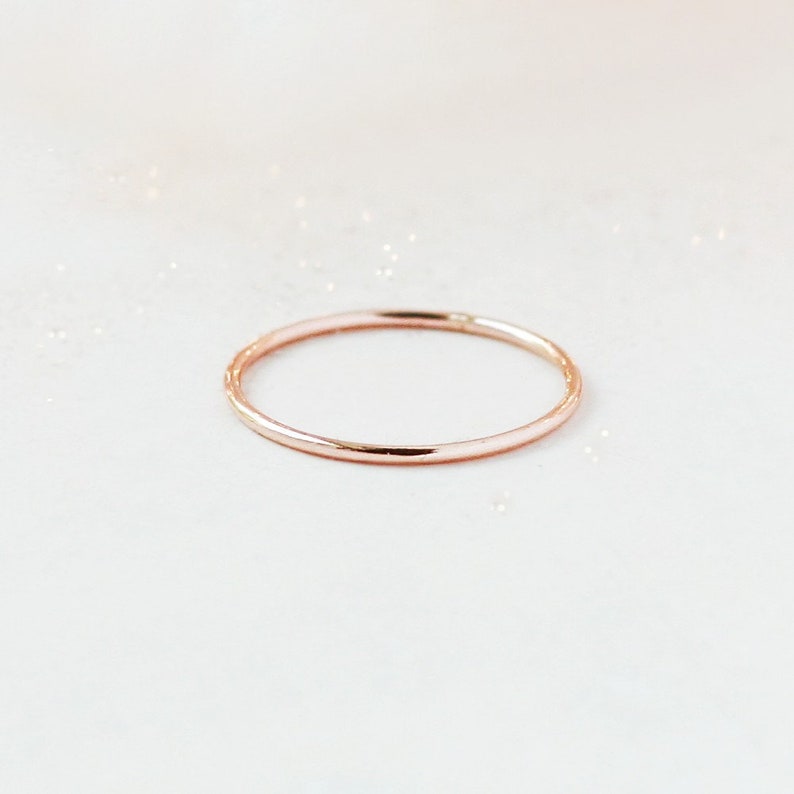 One slim 1 mm rounded finger ring band in 14k rose gold sits on a light off white background.