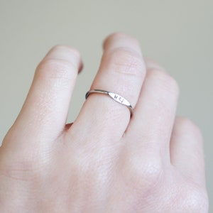 May include: A thin silver band ring with a flat, rectangular-shaped top engraved with the initials "H & J".