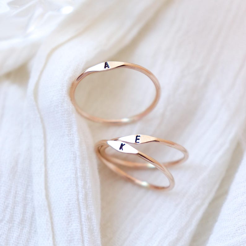 May include: Three gold-toned rings with the letters A, K, and E engraved on them. The rings are stacked on top of each other on a white surface.