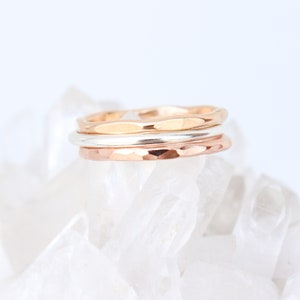 May include: Three hammered metal rings stacked on top of each other. The top ring is gold, the middle ring is silver, and the bottom ring is rose gold.