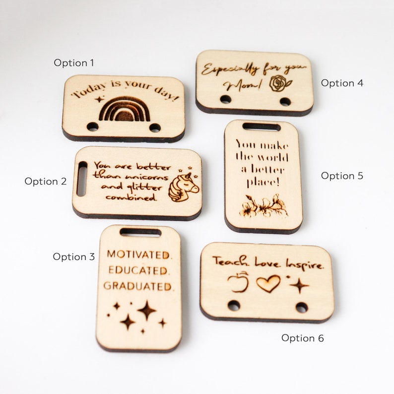 May include: A collection of six rectangular wooden tags with various engraved messages and designs. The tags include phrases like "Today is your day!" and "You are better than unicorns and glitter combined." Each tag has two holes.