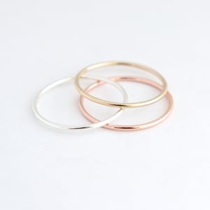 Set of three stackable rounded finger rings. One ring is 14k yellow fill gold, one ring is 14k rose fill gold and one solid sterling silver ring. All three rings are 1 mm thick.