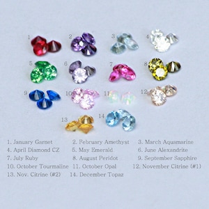 May include: A chart of birthstones for each month of the year. The chart shows a cluster of three gemstones for each month, with the month number and name listed above each cluster. The gemstones are arranged in rows of four, with the first row showing January Garnet, February Amethyst, March Aquamarine, and April Diamond CZ. The second row shows May Emerald, June Alexandrite, July Ruby, and August Peridot. The third row shows September Sapphire, October Tourmaline, October Opal, and November Citrine. The fourth row shows November Citrine and December Topaz.