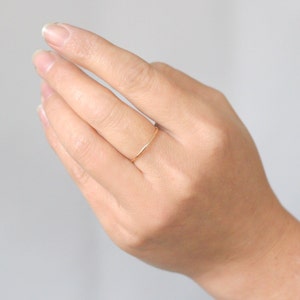 Woman's hand features a single 14k gold fill slim 1 mm rounded stacking band on the middle finger of the lady's hand.