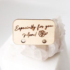 May include: A rectangular wooden tag with rounded corners, featuring the engraved text "Especially for you, Mom!" and a rose illustration. The tag has two small holes and is made of light-colored wood.