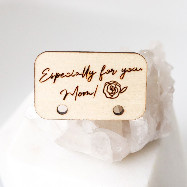 May include: A rectangular wooden tag with rounded corners, featuring the engraved text "Especially for you, Mom!" and a rose illustration. The tag has two small holes and is made of light-colored wood.