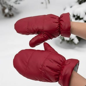 Può includere: Un paio di guanti imbottiti rossi. I guanti sono di una tonalità di rosso vibrante con una finitura lucida. I polsini sono di un colore grigio a contrasto. I guanti sono progettati per il calore e la protezione in caso di freddo.