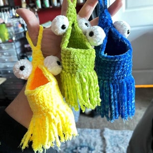 May include: Three crocheted hanging toy baskets with googly eyes and fringe. The baskets are yellow, green, and blue.