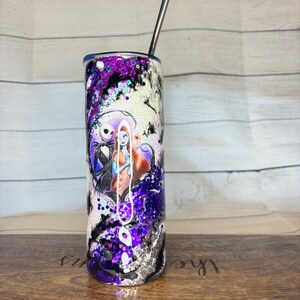 May include: A stainless steel tumbler with a black, white, and purple design featuring Jack Skellington and Sally from The Nightmare Before Christmas. The tumbler has a silver straw and is decorated with glitter.